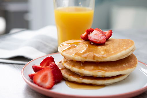 Morning breakfast of American style pancakes in a stack, sliced strawberries and orange juice