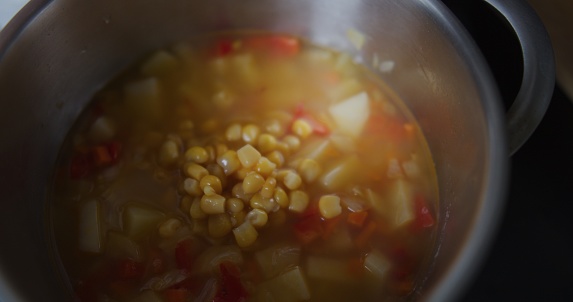 Making and serving vegetable soup in domestic kitchen. Part of a series: adding canned sweet corn