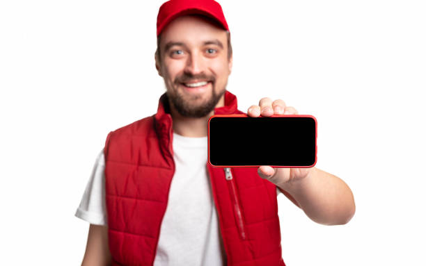 istock Cheerful delivery man showing smartphone to camera 1339066695
