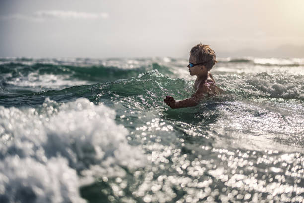 Teenage boy having fun in the sea. The boy is enjoying in the waves. Sunny summer day.\nCanon R5