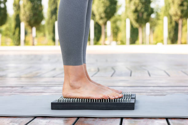 Yogi woman in gray pants standing barefoot on a wooden board with nails during outdoor yoga class Cropped shot of unrecognizable woman in grey pants standing barefoot on a wooden Sadhu board with nails during concentration meditation practice outdoors during morning yoga on fresh air bed of nails stock pictures, royalty-free photos & images