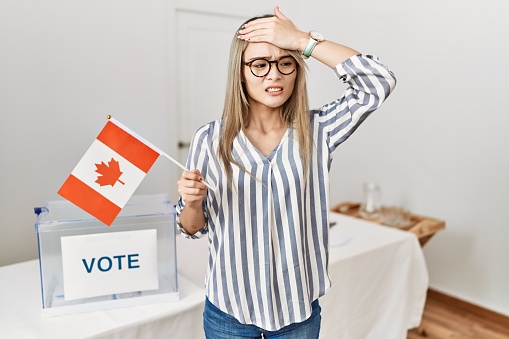 Asian young woman at political campaign election holding canada flag stressed and frustrated with hand on head, surprised and angry face
