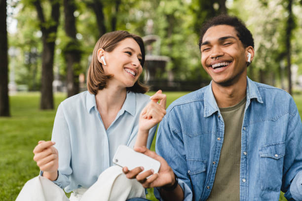 estudantes mestiços amigos casal romântico freelancers ouvindo o podcast música de rádio música música playlist música cantora em fones de ouvido earbuds usando aplicativo musical andando no parque da cidade ao ar livre - boyfriend heterosexual couple married activity - fotografias e filmes do acervo