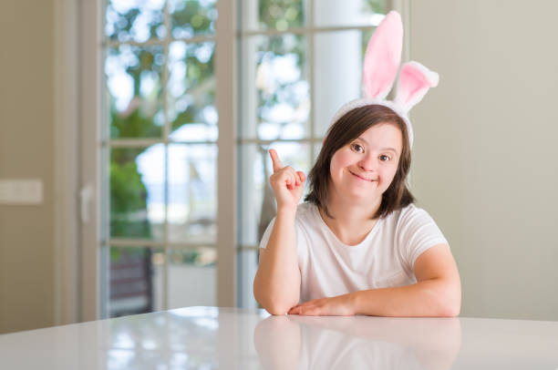 istock Down syndrome woman at home wearing easter rabbit ears surprised with an idea or question pointing finger with happy face, number one 1339075881