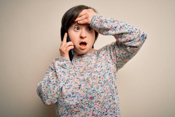istock Young down syndrome woman having a conversation speaking on smartphone stressed with hand on head, shocked with shame and surprise face, angry and frustrated. Fear and upset for mistake. 1339075891
