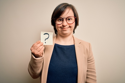 Young down syndrome business woman holding question mark paper as doubt symbol with a happy face standing and smiling with a confident smile showing teeth