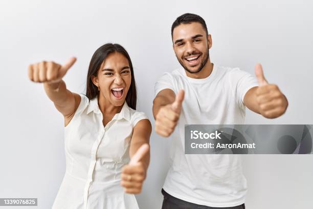 Young Interracial Couple Standing Together In Love Over Isolated Background Approving Doing Positive Gesture With Hand Thumbs Up Smiling And Happy For Success Winner Gesture Stock Photo - Download Image Now