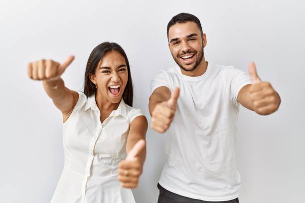 jovem casal interracial que se apaixona pelo fundo isolado aprovando fazendo gesto positivo com a mão, polegares para cima sorrindo e feliz pelo sucesso. gesto vencedor. - sinal de boas - fotografias e filmes do acervo