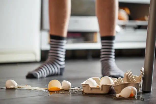 Photo of Broken eggs - accident at kitchen, mess. Legs on background