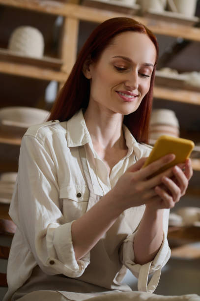 istock Young pretty woman with a smartphone in a pottery workshop 1339078677