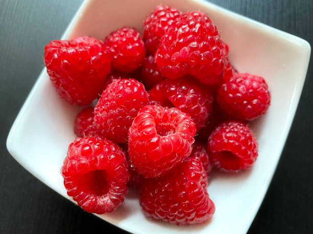 istock Red fresh juicy raspberry in white plate on gray black background. Fresh berries top view with copy space for text. 1339080578
