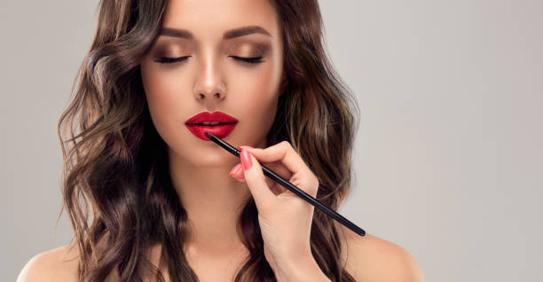 Hand of makeup artist is painting lips of model in a bright red color.Hairdressing art, hair dye and makeup. stock photo