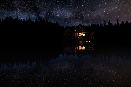 Luxurious Log Chalet by the Lake at Night. Sky and Milky Way Nature Photography. There is a perfect reflection of the stars in the lake.