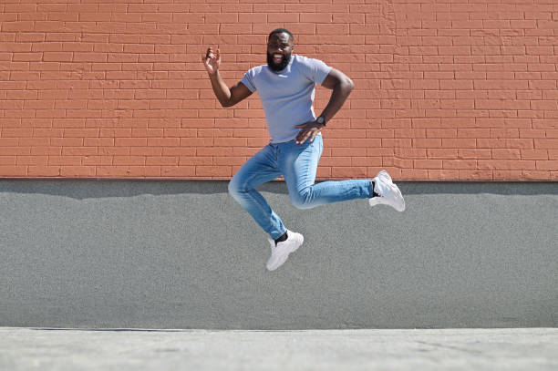 istock A dark-skinned man in a white tshirt and jeans jumping near the brick wall 1339085151