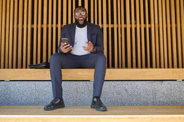 istock A dark-skinned man in a suit sitting on the bench with a smartphone in hands 1339085207