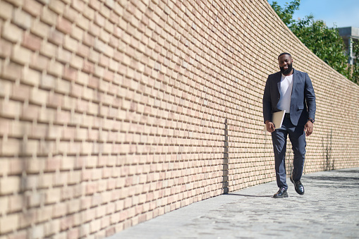 Street. A dark-skinned man walking along the brick wall