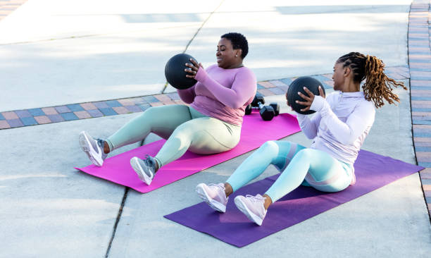 dos mujeres afroamericanas haciendo ejercicio con balón medicinal - pelota de ejercicio fotografías e imágenes de stock