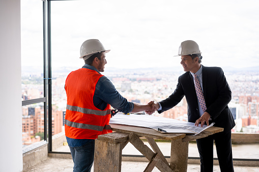 Happy Latin American housing developer greeting a building contractor with handshake at a construction site