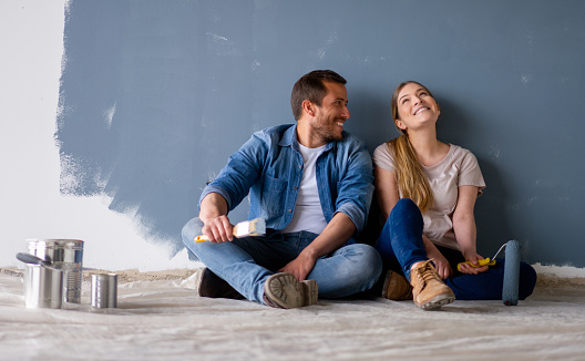 Loving Latin American couple having fun renovating their house and painting the walls and smiling while taking a break - home improvement concepts