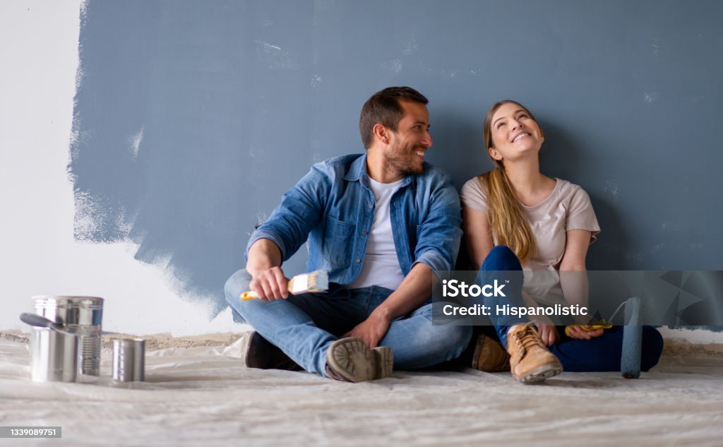 Loving couple having fun renovating their house and painting the walls Loving Latin American couple having fun renovating their house and painting the walls and smiling while taking a break - home improvement concepts Couple - Relationship Stock Photo