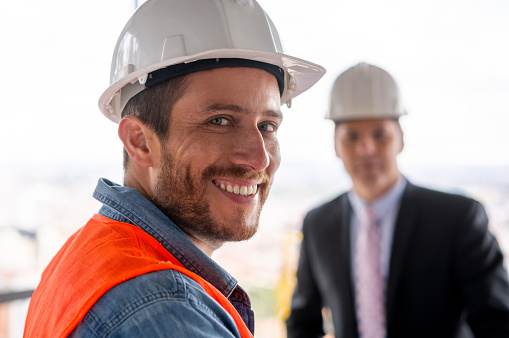 Woman architect showing blueprint to general contractor, asking for advice and discussing detail before building start, coming at construction site