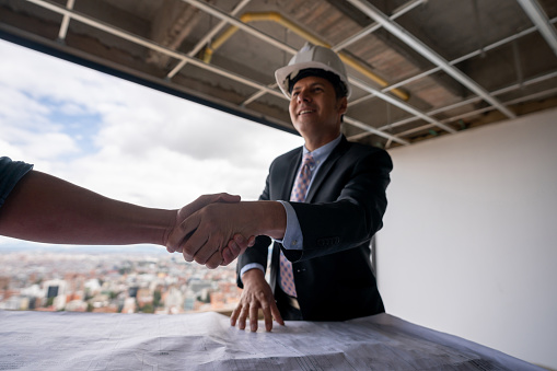 Close-up on a happy architect greeting client with handshake at a construction site and smiling