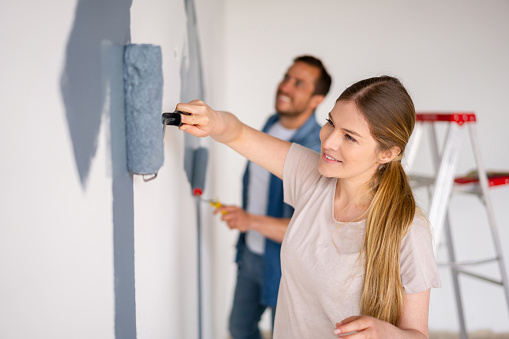 Happy Latin American couple remodeling their house and painting the walls with a grey color - home improvement concepts