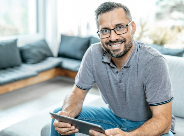 istock Middle aged man sitting on sofa, reading on tablet 1339094388