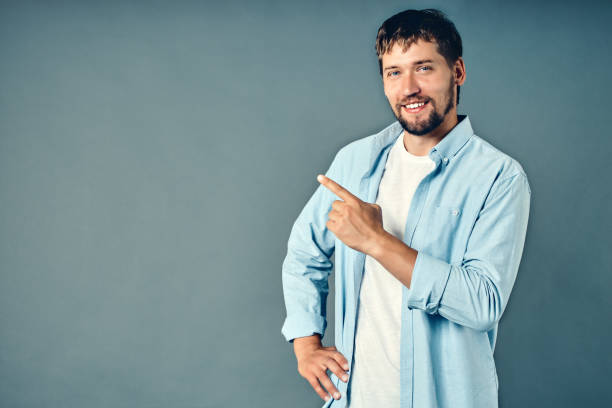 istock A young Caucasian guy with a beard smiles and points his finger to the side of the empty space 1339096607