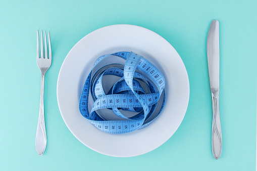 A centimeter on a white plate, fork and knife. Turquoise background. Diet concept.