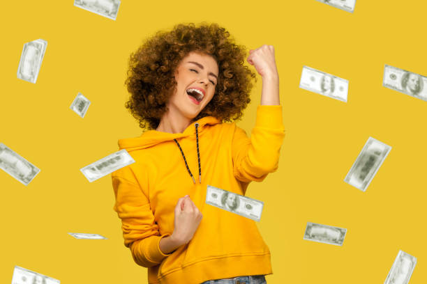Money rain. young woman celebrating richness and enjoying. Money rain. Yes I did it! Portrait of joyous winner rich young woman in yellow hoody standing screaming and closed eyes, celebrating victory and richness. indoor isolated on yellow background money rain stock pictures, royalty-free photos & images
