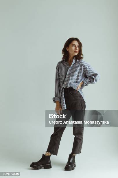 A Girl In A Mans Loose Shirt Chelsea Boots And Jeans Stands In A White Studio Stock Photo - Download Image Now