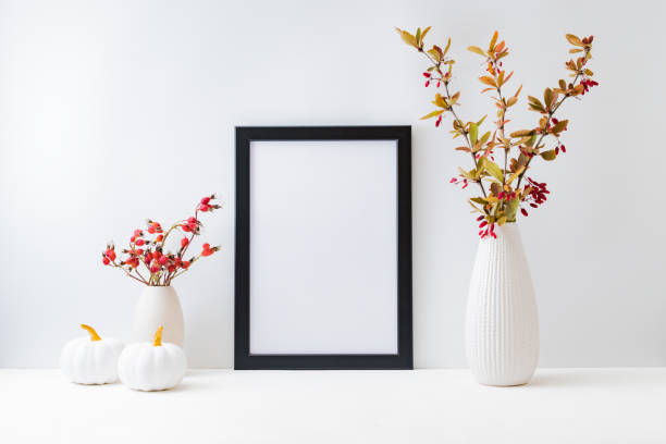 istock Home interior with decor elements. Mockup with a black frame, colorful autumn leaves and red berries in a vase on a light background 1339120197