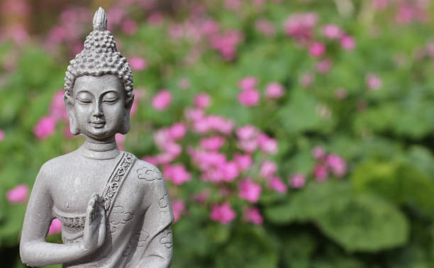 พระพุทธรูปในสวนที่มีพื้นหลังดอกไม้สีชมพูเบลอ - buddha face ภาพสต็อก ภาพถ่ายและรูปภาพปลอดค่าลิขสิท��ธิ์