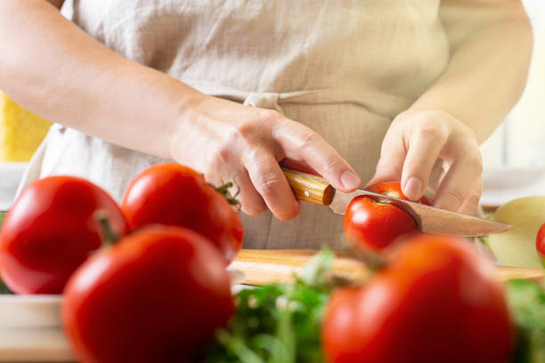 istock Chef slicing tomato using knife on the table in restaurant. Process of cutting and preparation food in kitchen. 1339131194