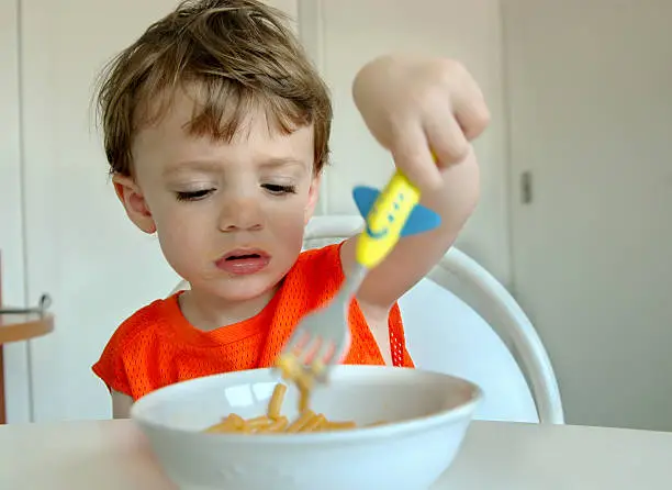 A little boy picks at his food with a fork.