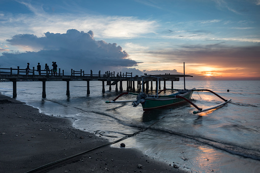Colorful sunset at Lovina beach located in Bali Indonesia with a pier facing the ocean.