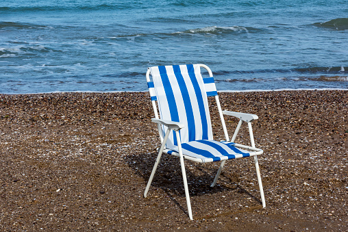 Blue striped deck lounge chair on the sand and in the water reflection on the seaside in Turkey.