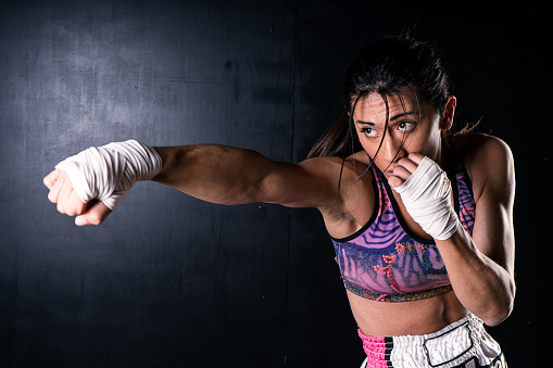 Young latin woman practicing boxing and kickboxing. She scores a direct punch with her fist. Differential focus. Sport, fitness, training concept.