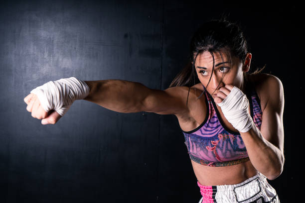 Young latin woman practicing boxing and kickboxing. She scores a direct punch with her fist. Differential focus. Sport, fitness concept. Young latin woman practicing boxing and kickboxing. She scores a direct punch with her fist. Differential focus. Sport, fitness, training concept. kickboxing photos stock pictures, royalty-free photos & images