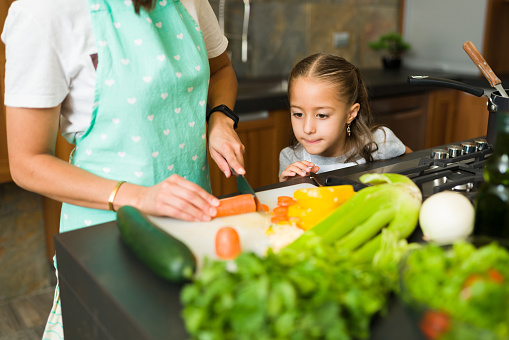 Close up of a cute little girl watching her mom chopping vegetables to prepare a delicious soup for lunch