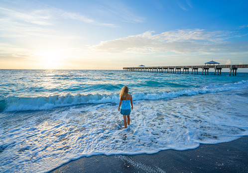 Woman relaxing at sunrise on the beach. Girl enjoying vacation, wading in the ocean. Woman walking on the beach. Summer beach scenery. Juno Beach, Florida, USA.