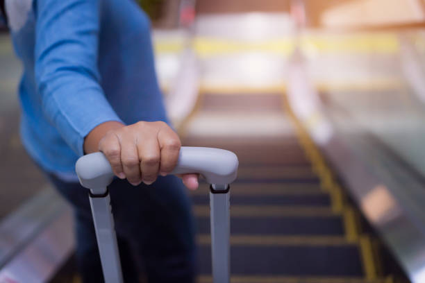 mulher viajante segura bagagem em escada rolante no aeroporto terminal ou voo de trânsito com mala em férias de viagem no aeroporto internacional de chegada de elevador, estilo de vida de avião na ásia - escalator elevator women leaving - fotografias e filmes do acervo