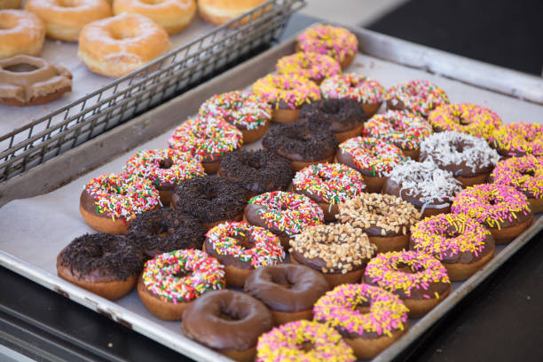 Metal trays of rows of doughnuts with glaze and sprinkles stock photo