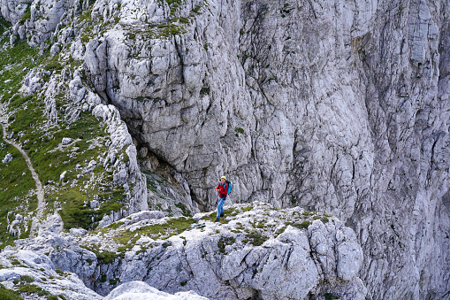 View of Mature woman walking  at edge of rock above 2000 m at one of  the most photogenic locations in Julian Alps.  She is on top of rock,  with helmet on her head an is looking to the landscape between rocks.