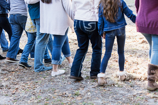 Cropped rear view of a large multi-generation Hispanic family walking in the park, side by side, holding hands. They are unrecognizable, visible only from the shoulders down. They range in age from 7 years to early 70s.