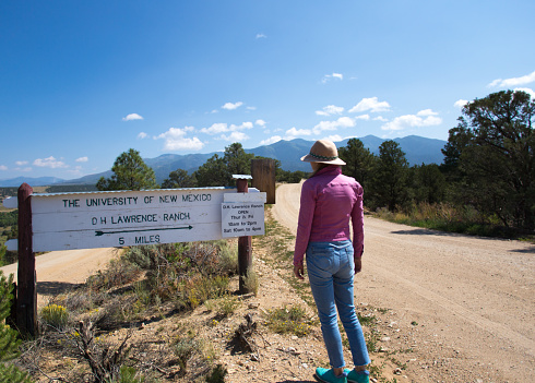 San Cristobal, NM: Tourist looking at directional sign to the D. H. Lawrence Ranch, located 15 miles outside Taos. Lawrence lived there in 1924-1925.