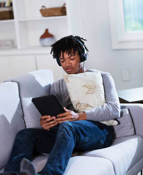 istock Young black man with headphones uses digital tablet on sofa 1339174118