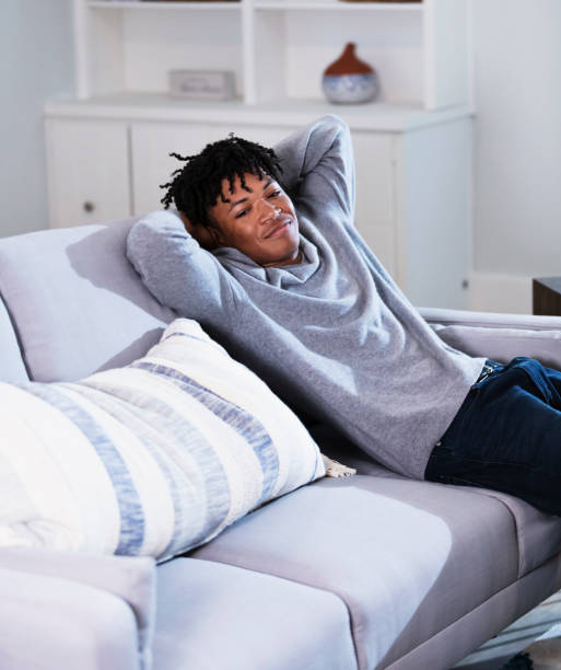 istock Young black man relaxing on sofa with hands behind head 1339174126