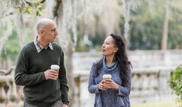 interracial couple walking in park, talking over coffee - common serious couple men imagens e fotografias de stock